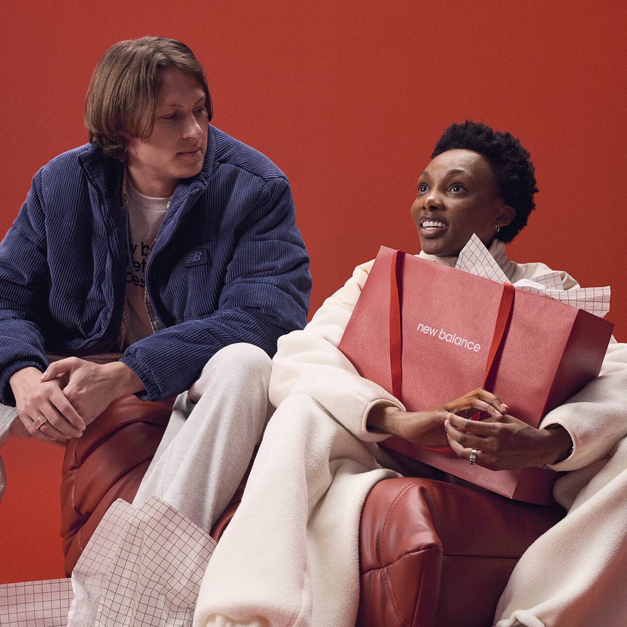 A woman smiling and holding a red New Balance giftbag with a man looking at her.